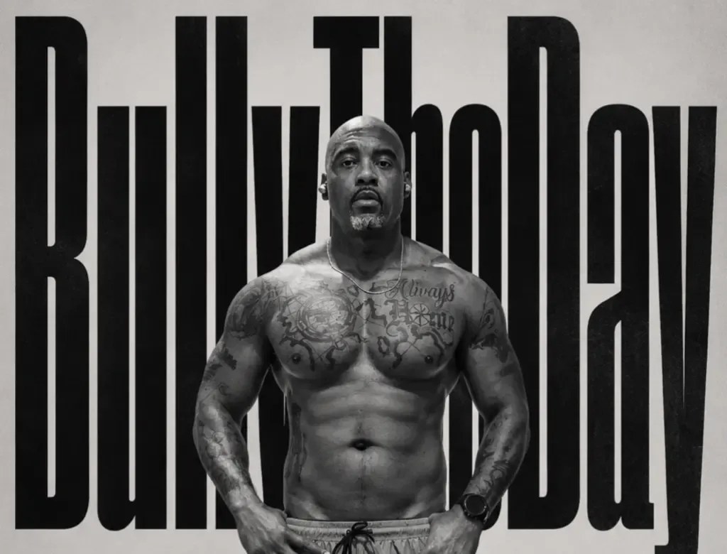Fred B., shirtless in black and white, standing in front of the words Bully The Day